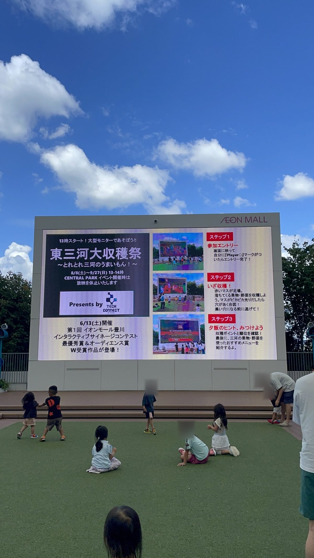 イオンモール豊川のサイネージに、東三河大収穫祭の遊び方と、コンテストでのダブル受賞作品であることを知らせる画面が映っている