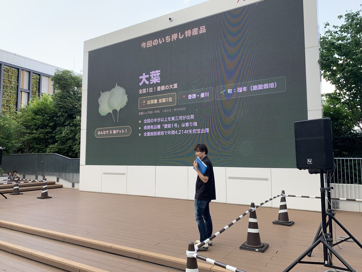 サイネージに東三河の特産品「大葉」を紹介する画面が映り、ステージで水野真治が説明している