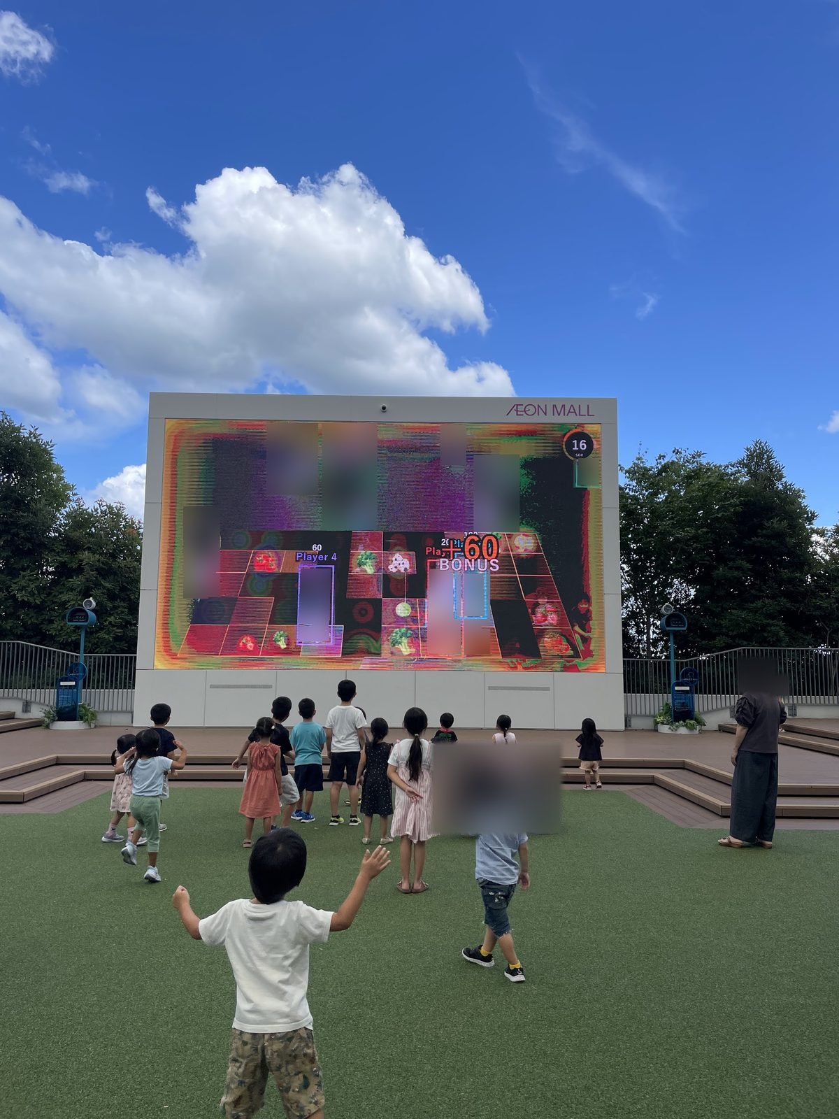 イオンモール豊川の400インチサイネージの前で、体を動かしてARゲームを遊ぶ子どもたちの後ろ姿